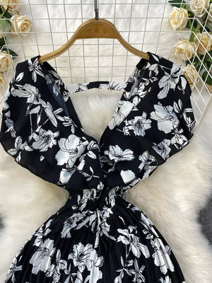 Black floral print maternity romper with wide legs and pleated skirt.
