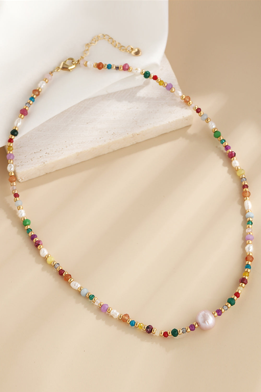 Multicolor beaded gemstone and pearl necklace with gold accents and a large pearl accent.