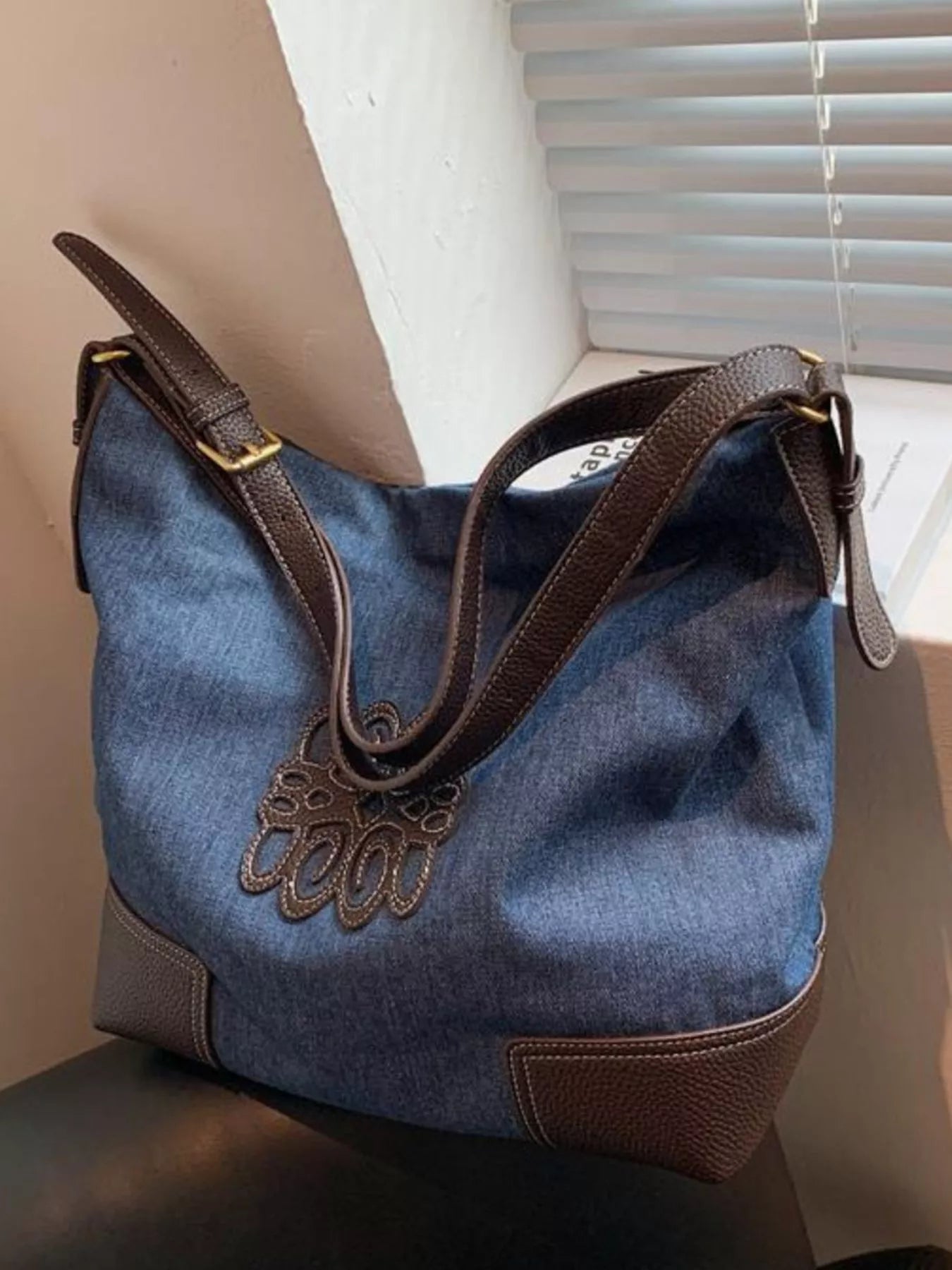 Blue denim shopper bag with brown leather trim and decorative cutout detail.
