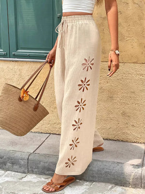 Cream linen wide-leg pants with floral cutouts and drawstring waist.