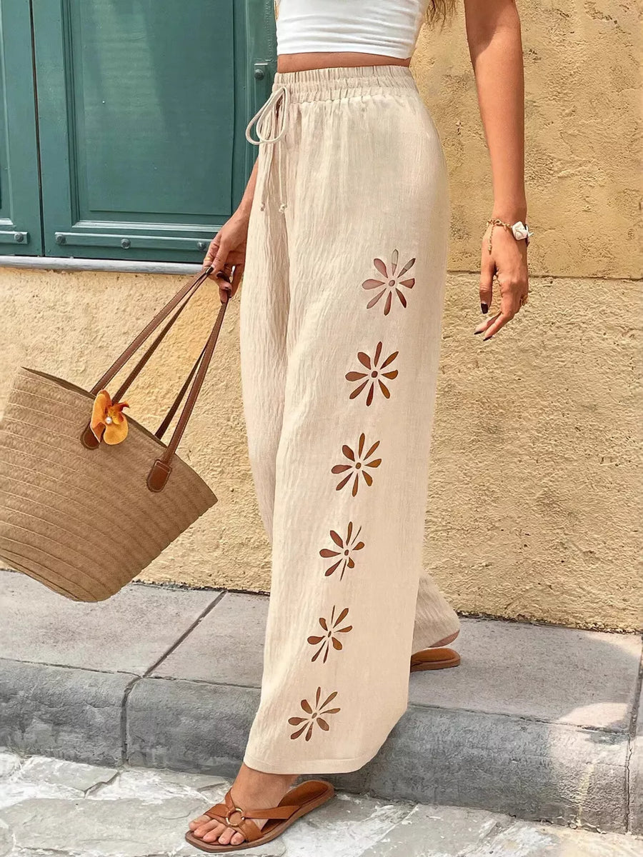 Cream linen wide-leg pants with floral cutouts and drawstring waist.