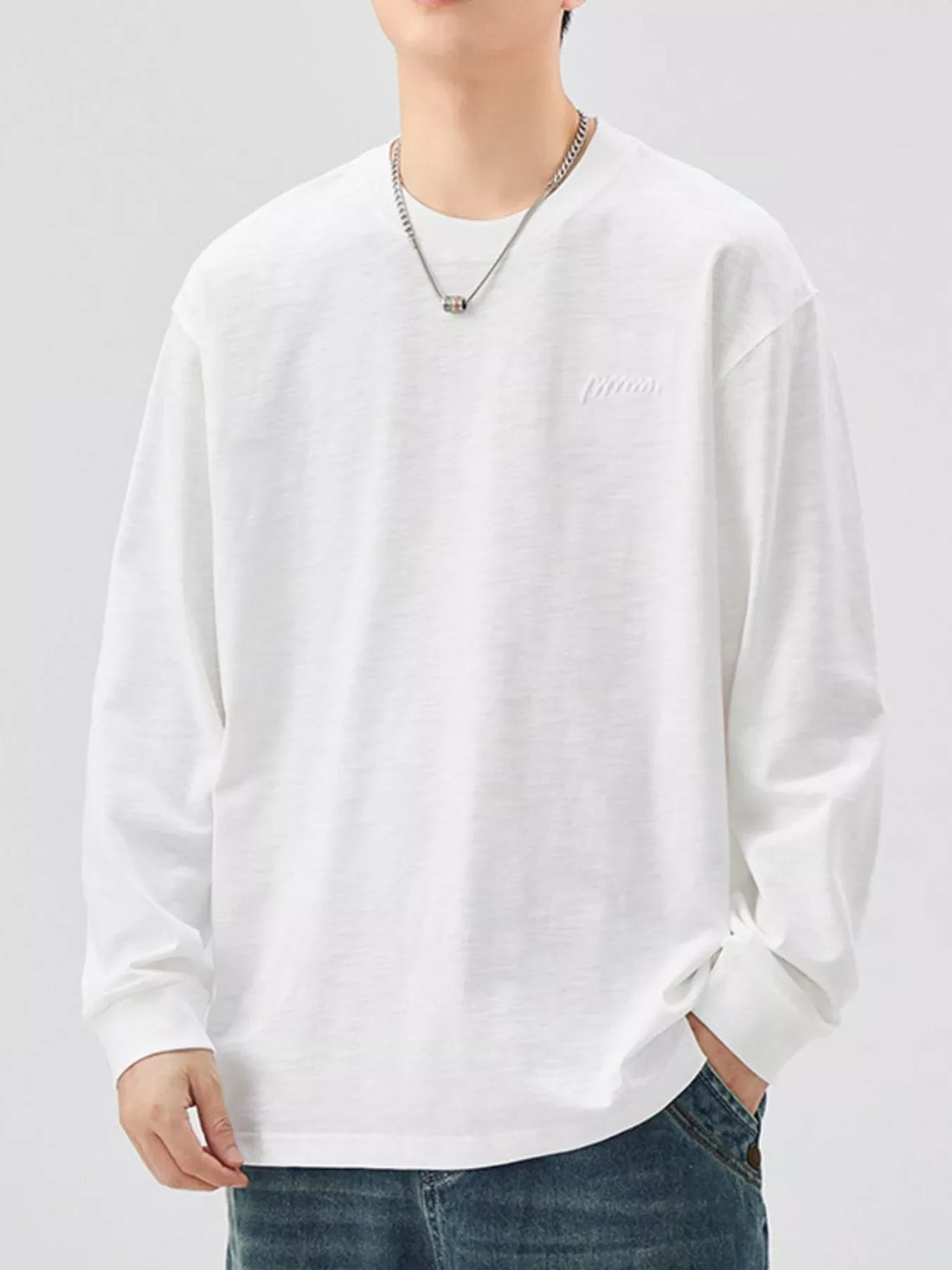 Oversized white cotton long-sleeve tee with subtle embroidered logo detail