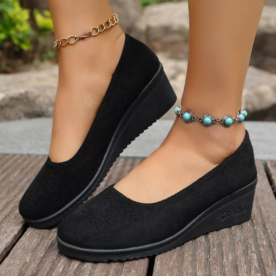Black textured round toe wedge slip-ons with a low wedge heel.