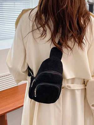 Black corduroy sling bag with two zip pockets worn crossbody.