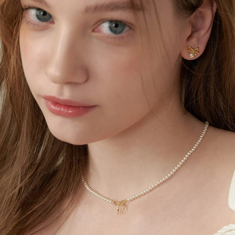 Gold bow pendant necklace with pearls, styled as a choker.