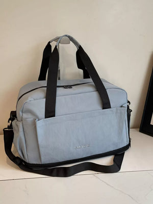 Light blue Oxford cloth travel tote bag with black straps and zippered front pocket.