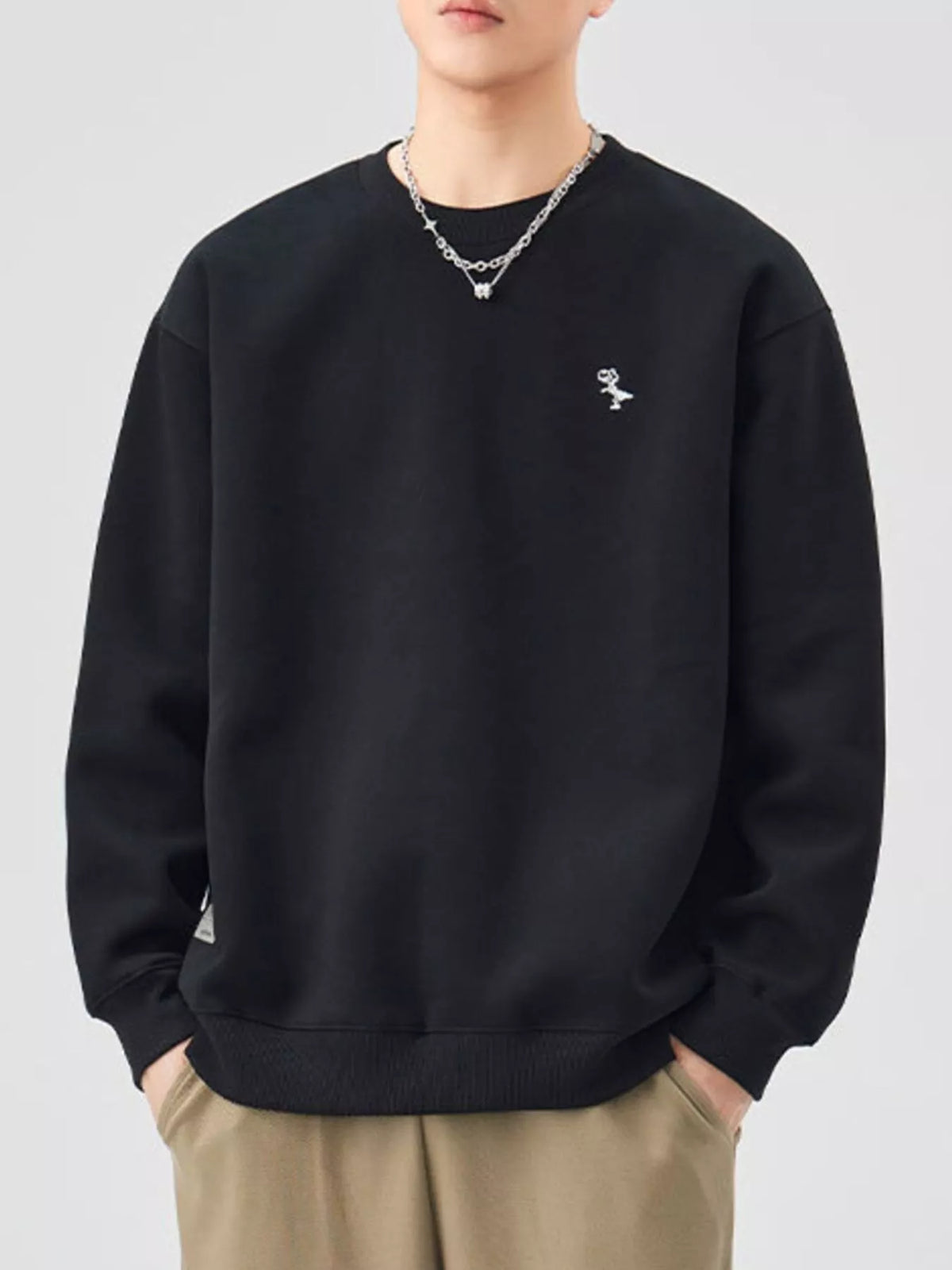 Black long-sleeve sweatshirt with crew neck and small embroidered dinosaur detail.
