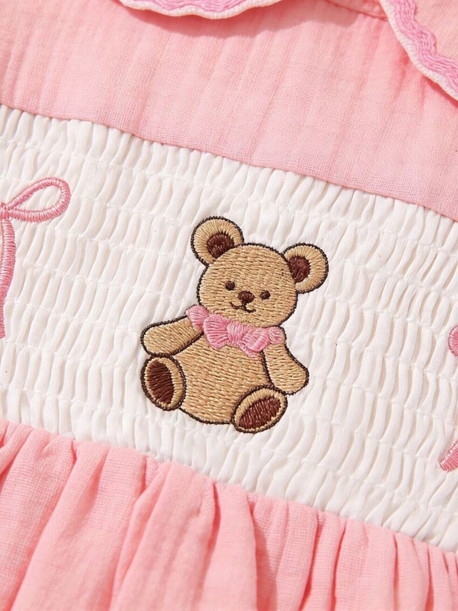 Embroidered teddy bear baby dress in pink and white cotton with smocking detail.