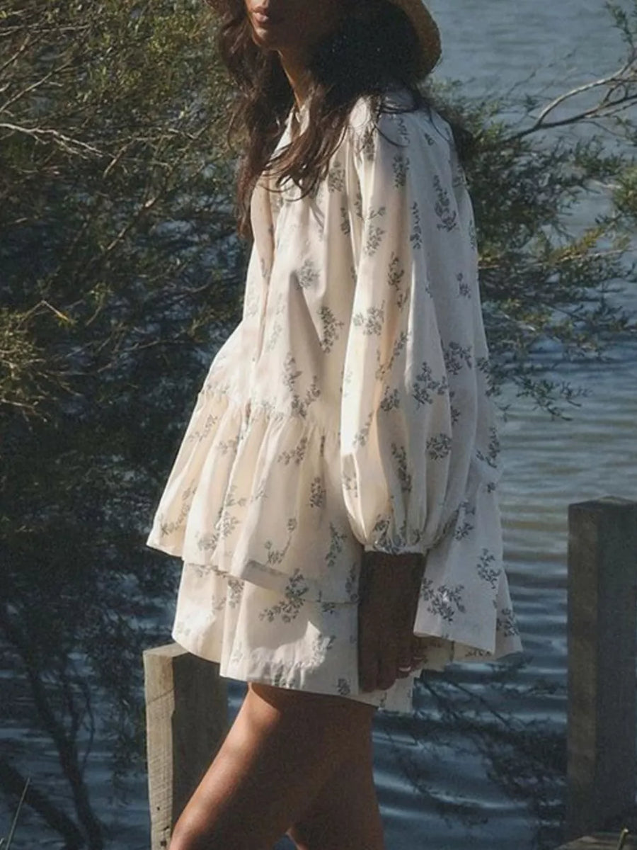 Tiered mini dress in cream with a blue floral print, featuring voluminous sleeves and a ruffled hem.