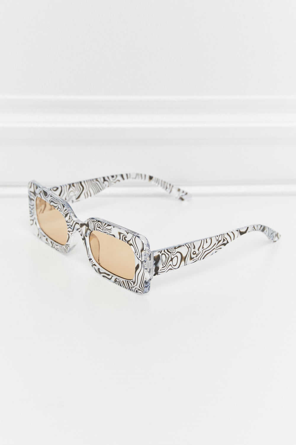 Rectangular frame sunglasses with a black and white swirl print and tan lenses.