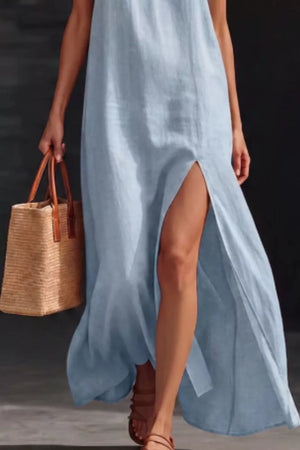 Light blue V-neck maxi dress with high slit, sleeveless, and a straw tote bag.