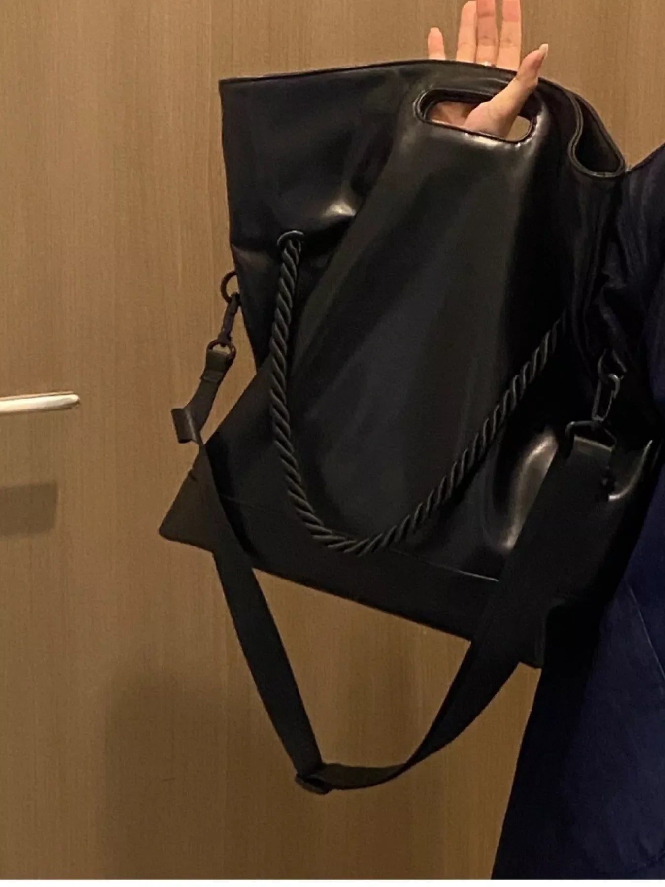 Black oversized PU leather tote bag with rope detail and crossbody strap.