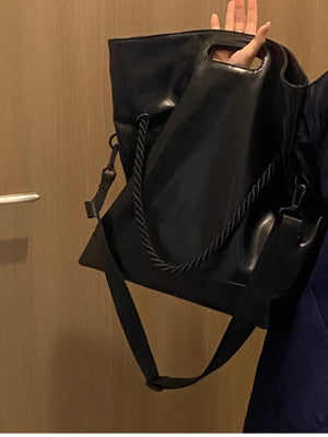 Black oversized PU leather tote bag with rope detail and crossbody strap.
