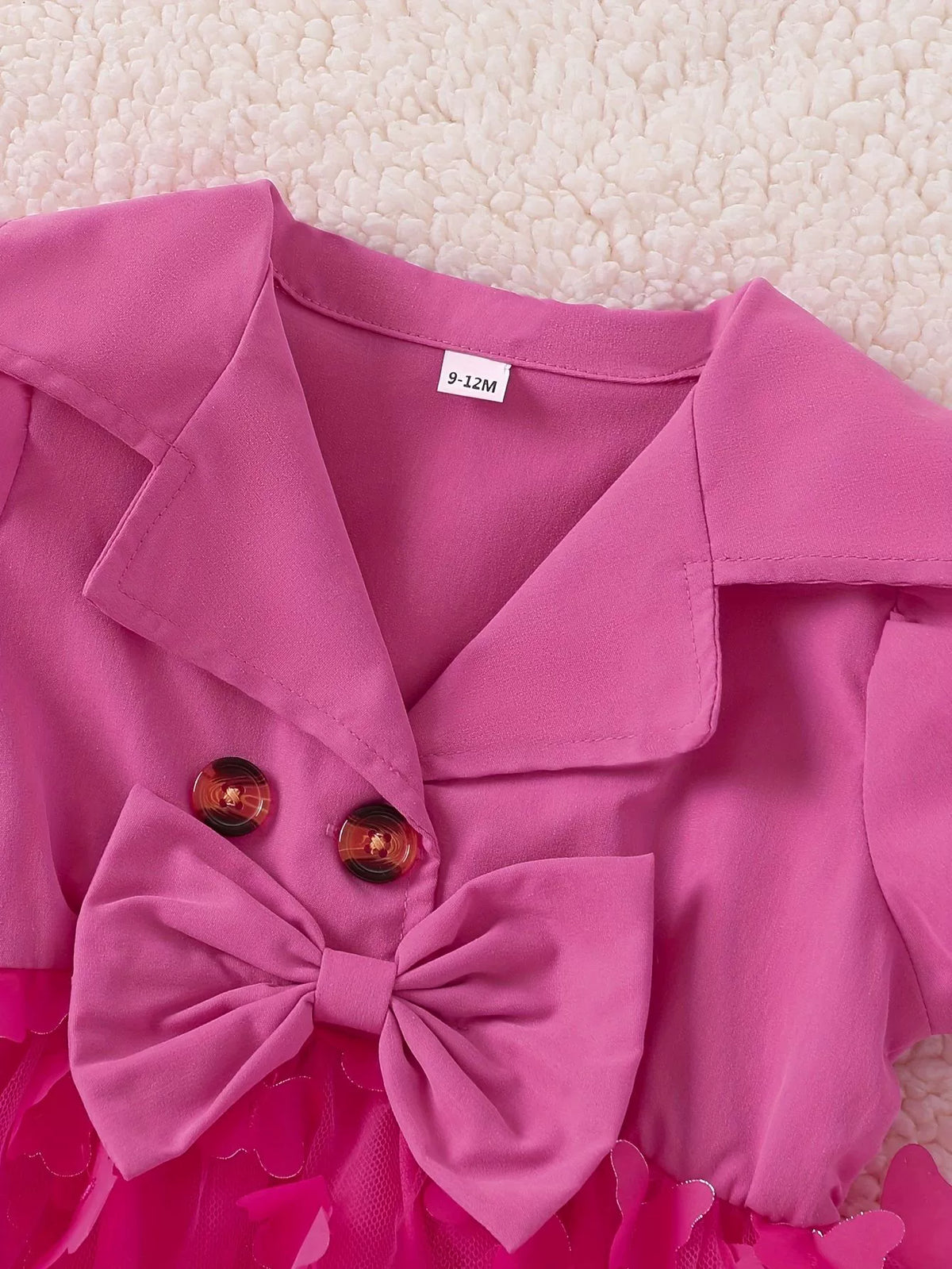 Pink baby dress with collared neckline, bow, buttons, and butterfly applique tulle skirt.