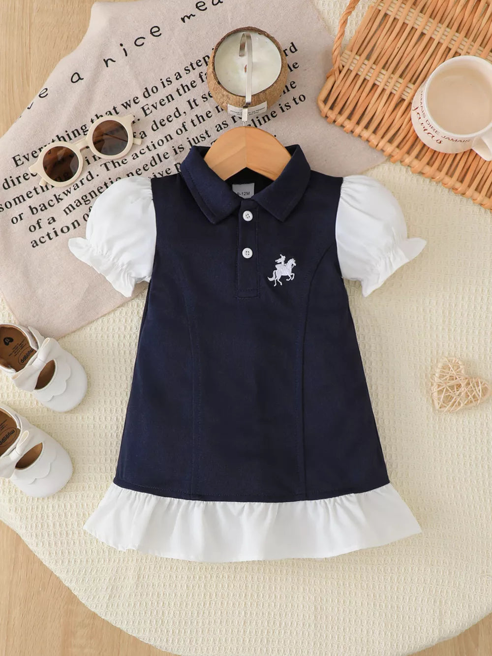 Baby navy polo dress with white ruffled hem, puff sleeves, and horse embroidery.