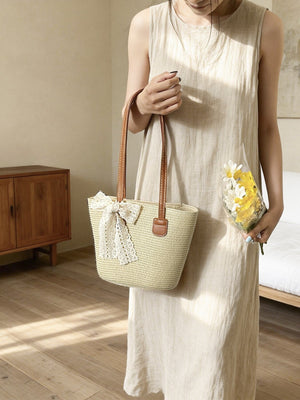 Charming straw shoulder bag in off-white with lace bow detail and leather handles.