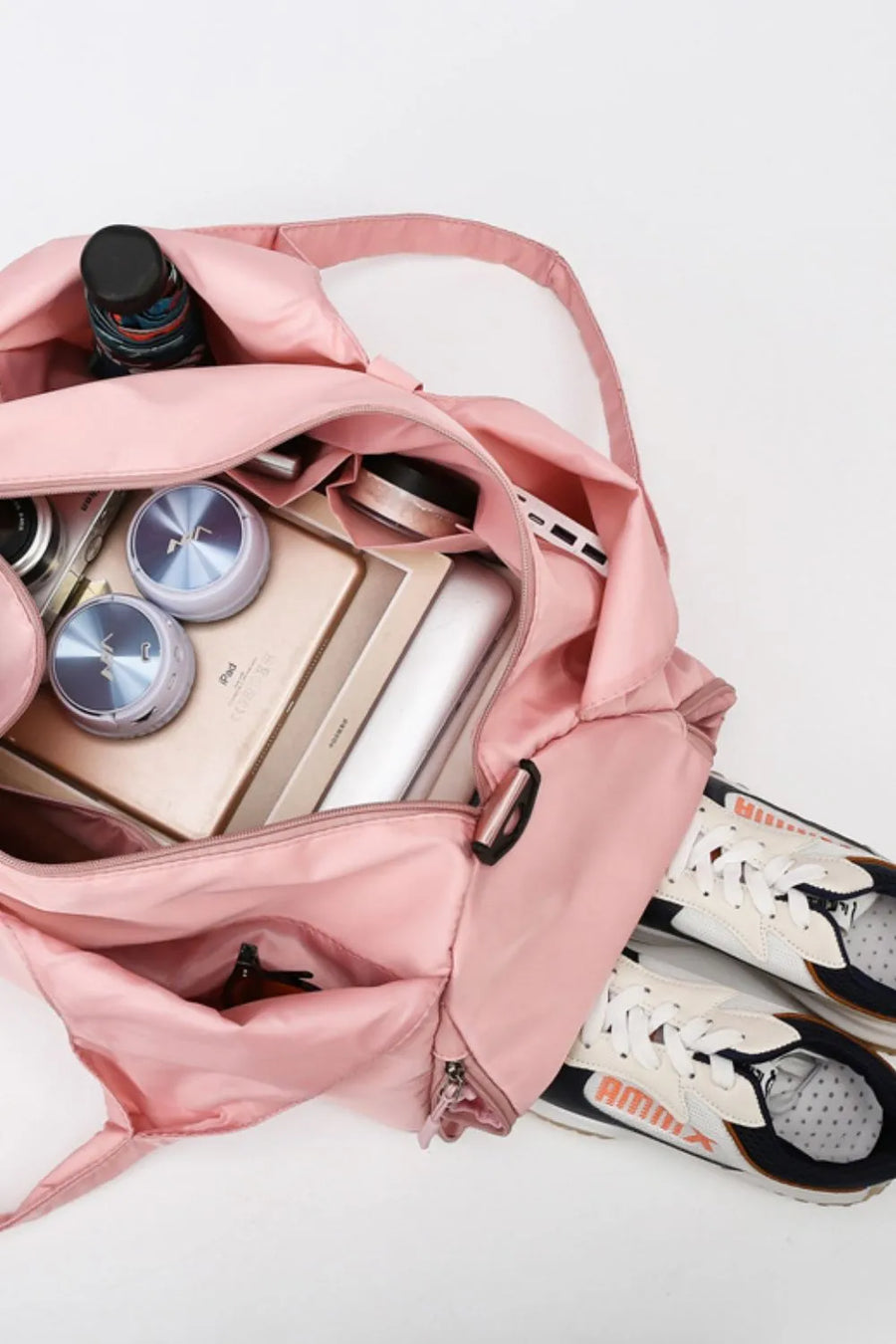 Dusty Pink duffel bag packed with essentials including a tablet, speakers, and a camera, with sneakers beside it.