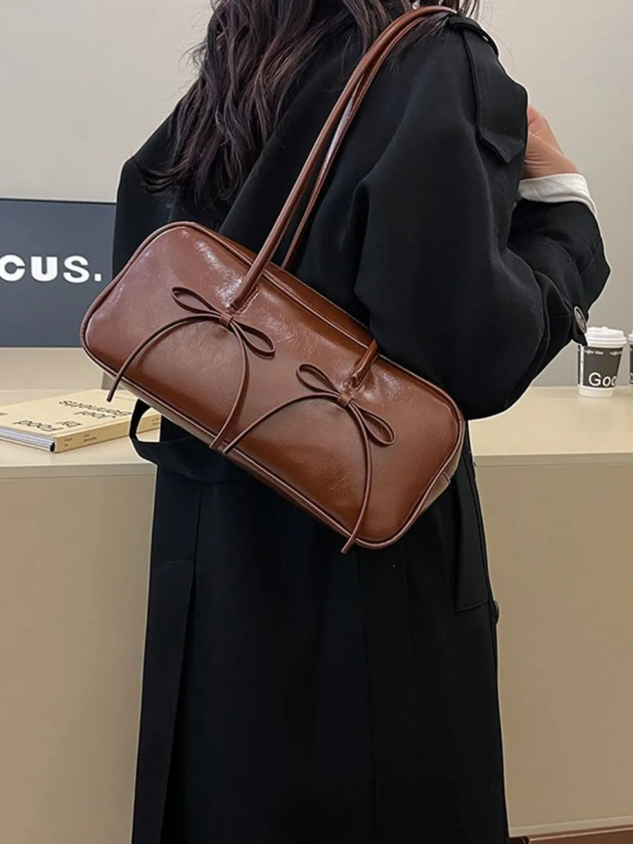 Brown patent leather shoulder bag with bow details and a top handle.