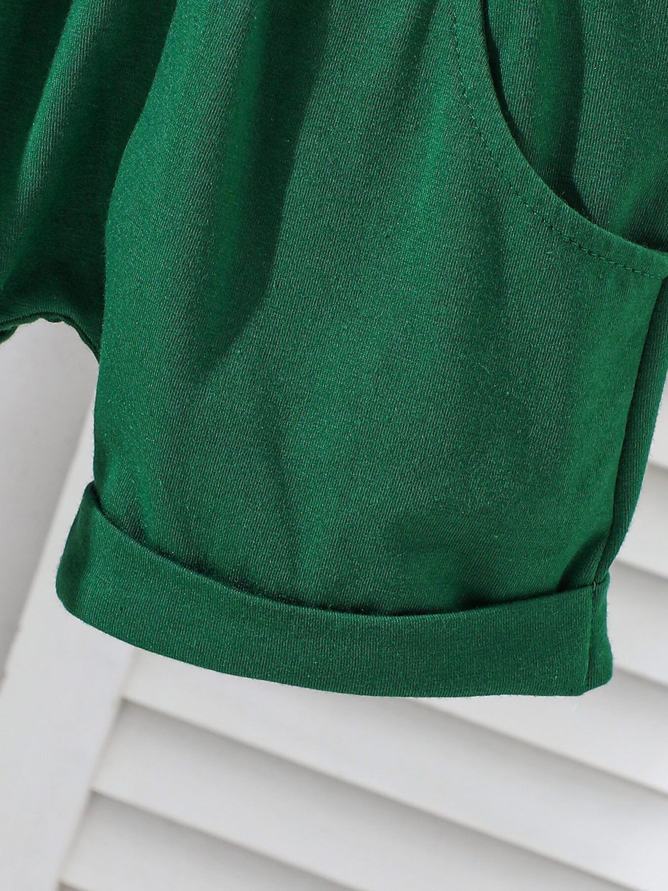 Dark green cotton baby shorts with cuffed hem and pocket detail.