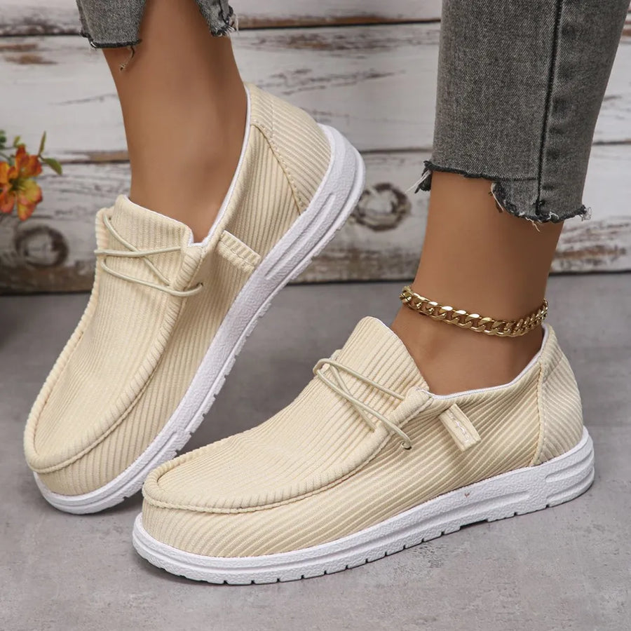 Beige textured slip-on espadrille sneakers with white soles and decorative laces.