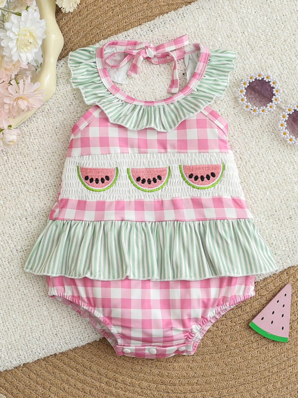 Baby one-piece swimsuit with pink gingham, smocked panel with watermelon appliques, and green stripe ruffles.