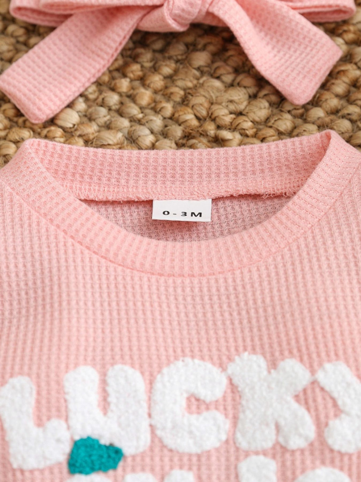 Pink waffle knit baby one-piece with white chenille "Lucky" lettering and a matching headband.