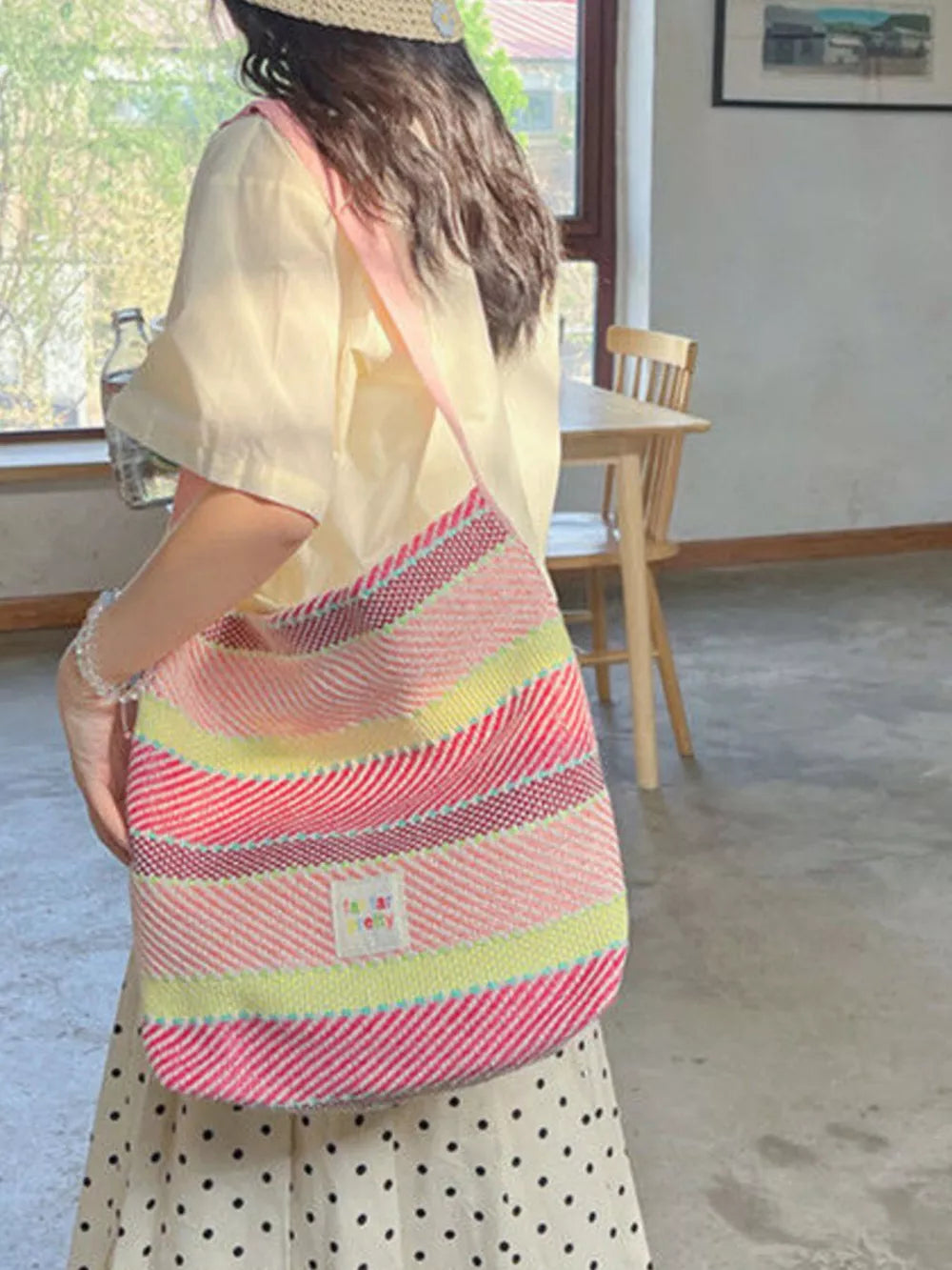 Vibrant striped woven shoulder bag with pink strap and a small white tag.