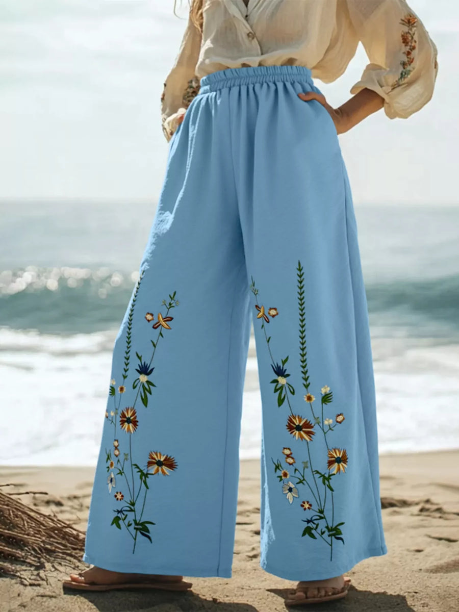 Sky blue wide-leg trousers with embroidered floral details and an elastic waistband.