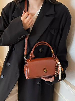 Brown leather crossbody bag with beaded charm and gold clasp detail