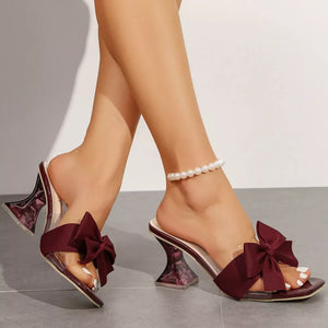Burgundy bow open-toe sandals with clear strap and sculpted heel.