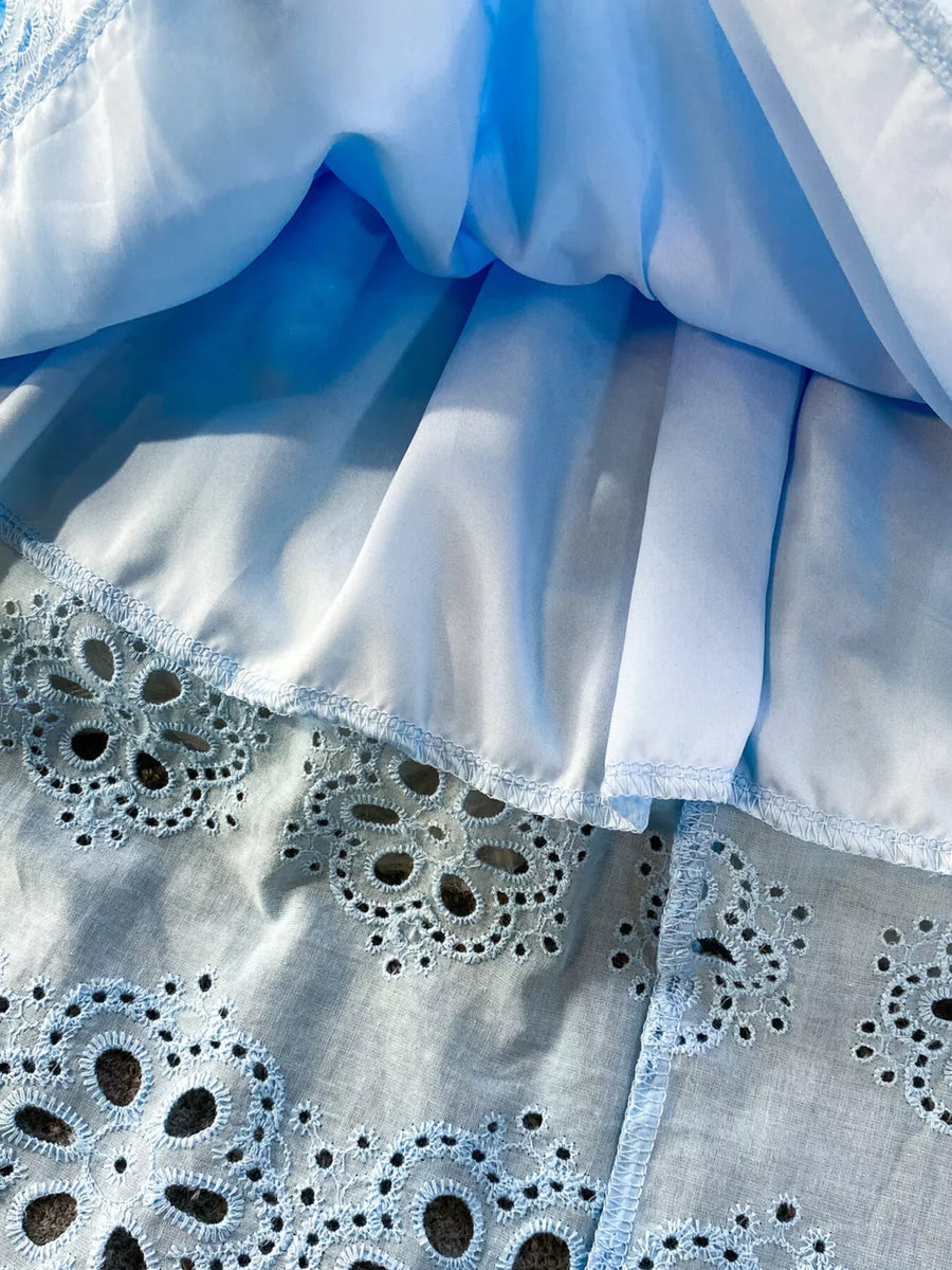 Blue eyelet maxi dress with intricate floral cutouts and a ruffled hem detail.