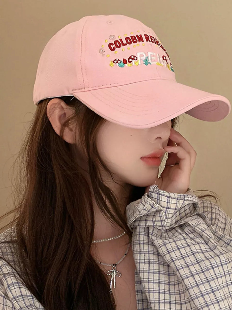 Blush pink baseball cap with playful mushroom embroidery and text detail.