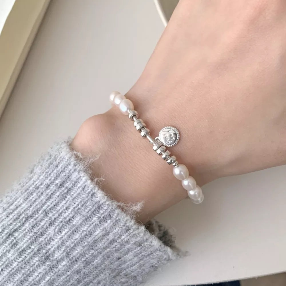 Delicate freshwater pearl and silver bracelet with a round charm on a wrist.