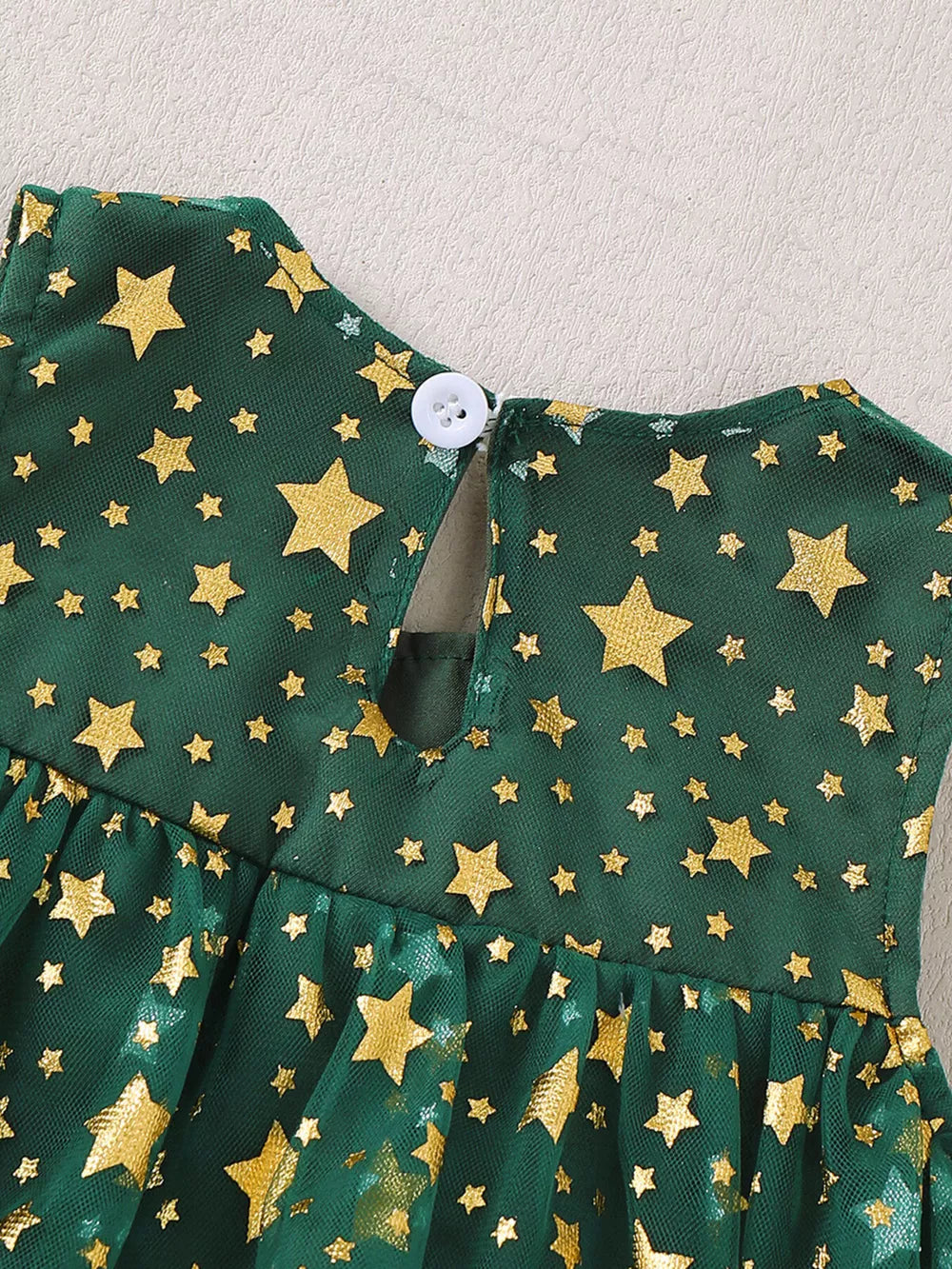 Green tulle baby dress with gold stars and a white button closure.