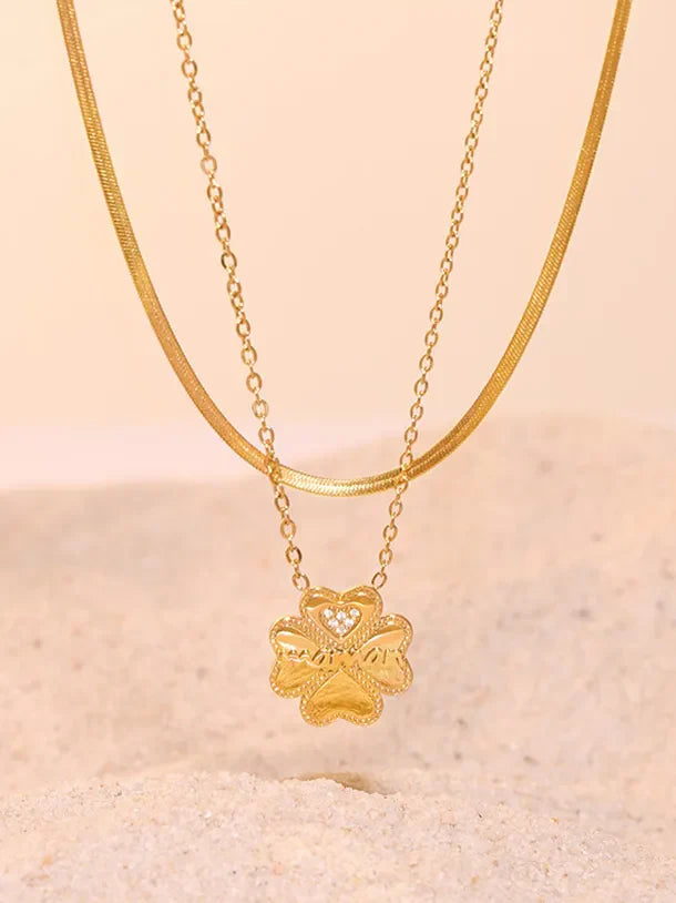 Gold layered necklace with a clover charm featuring a heart detail and small stones.