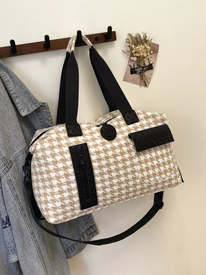 Chic houndstooth duffle bag with black accents and detachable strap.