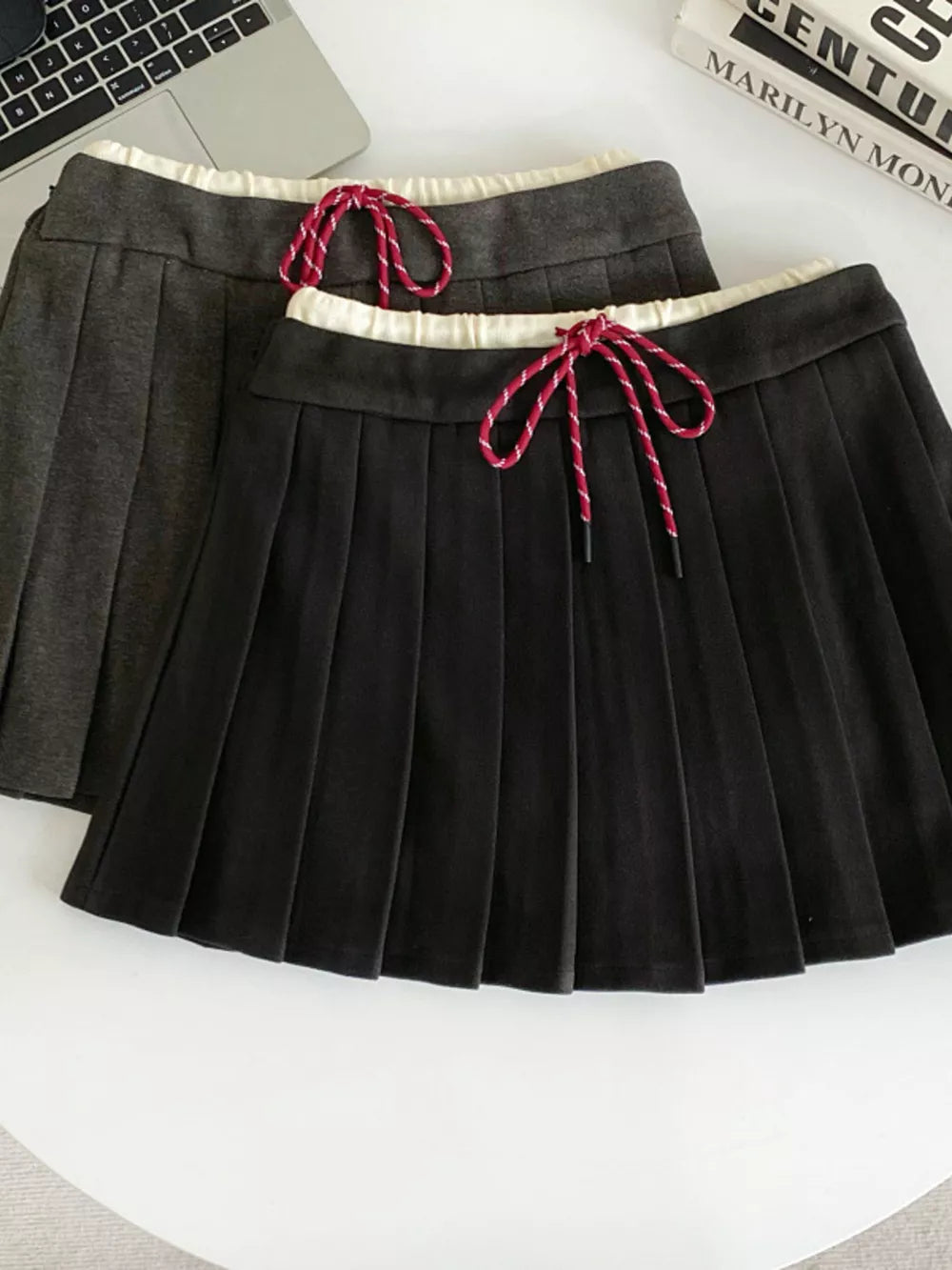 Chic pleated skirt in black and dark gray with drawstring waist and white trim.