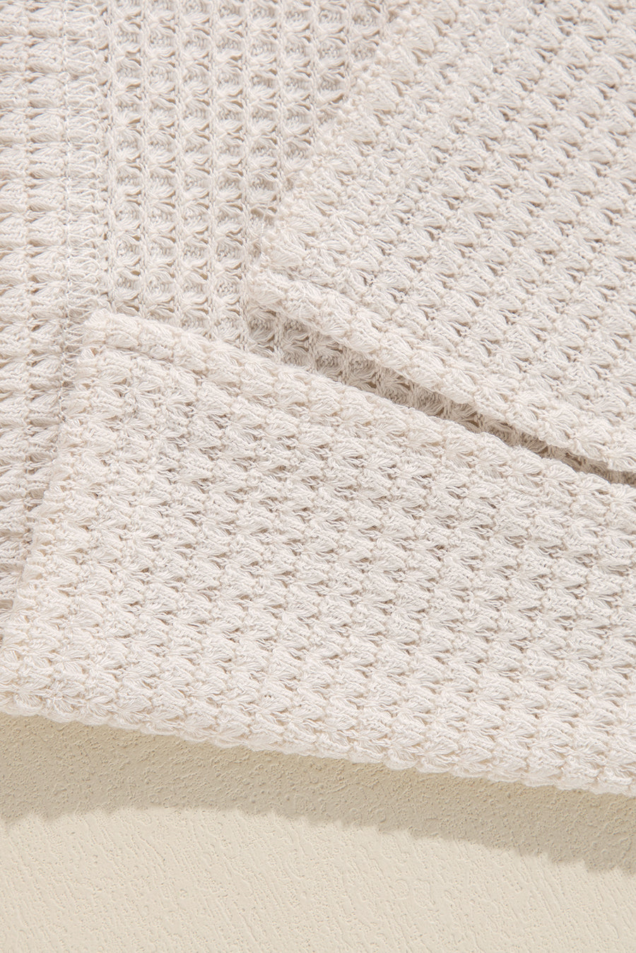 Beige waffle knit V-neck top with slit hem detail.