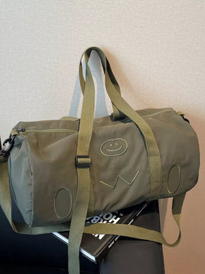 Green duffle bag with adjustable strap and embroidered smiley face detail