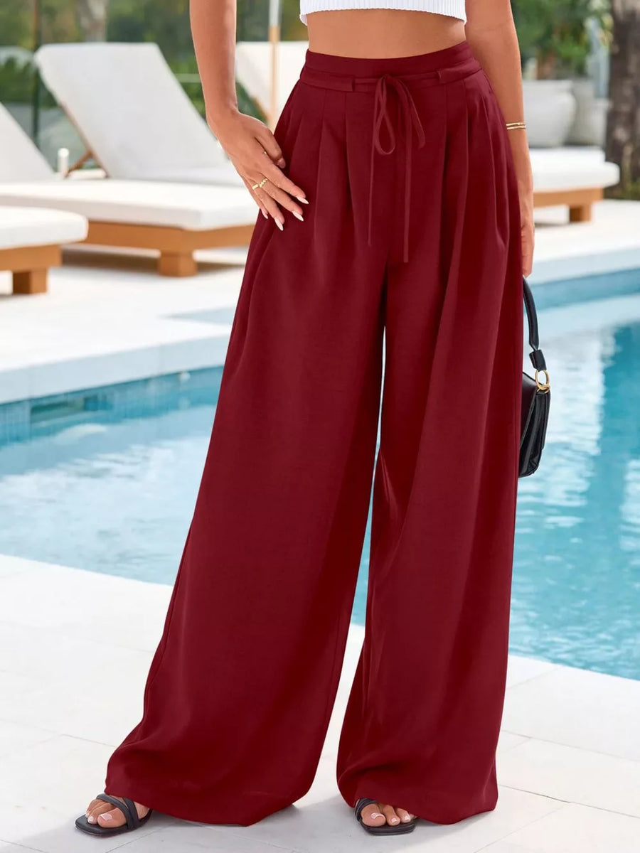 Burgundy high-waisted pleated wide-leg pants with drawstring and pockets.