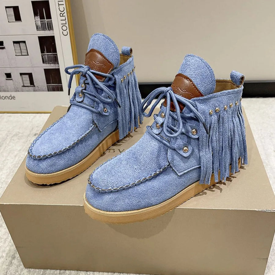 Blue denim moc-toe ankle boots with fringe and stud details.