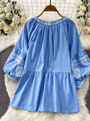 Blue tie-neck blouse with intricate white embroidery on neckline and balloon sleeves.