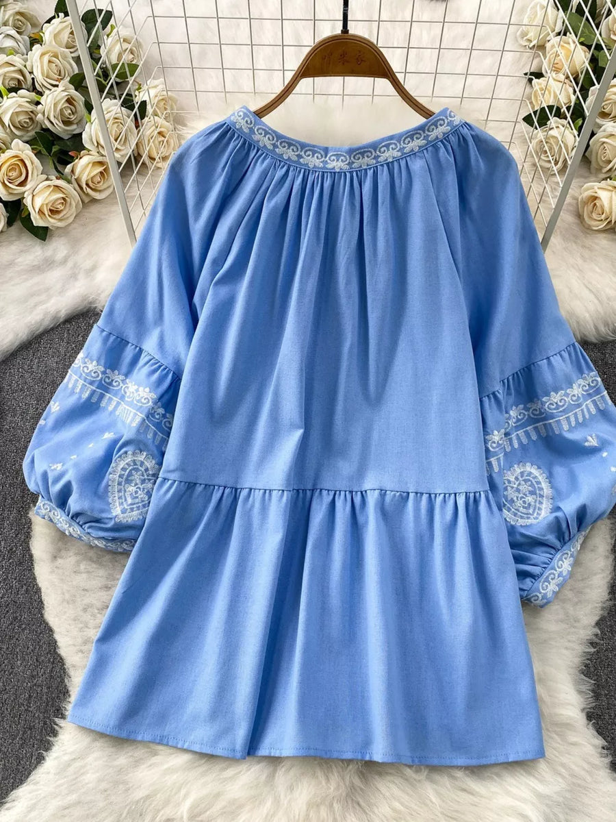 Blue tie-neck blouse with intricate white embroidery on neckline and balloon sleeves.