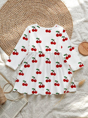 White baby dress with allover red cherry print, long sleeves, and gathered waist.