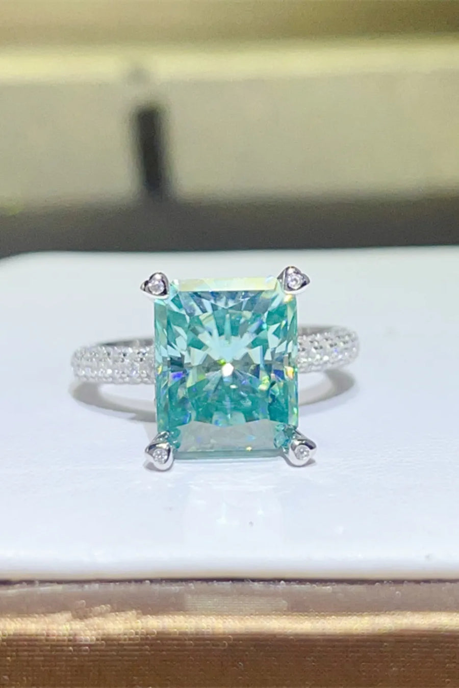 Teal radiant cut emerald ring with pave band and diamond prongs
