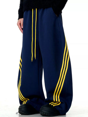 Men's navy blue wide-leg sweatpants with yellow side stripes and drawstring waist.
