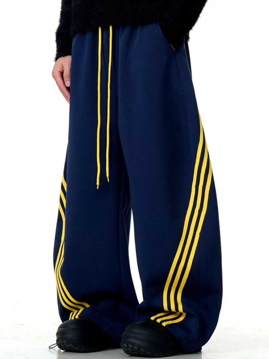Men's navy blue wide-leg sweatpants with yellow side stripes and drawstring waist.