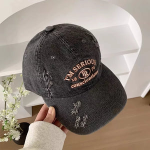 Distressed black denim baseball cap with embroidered text and distressed details.