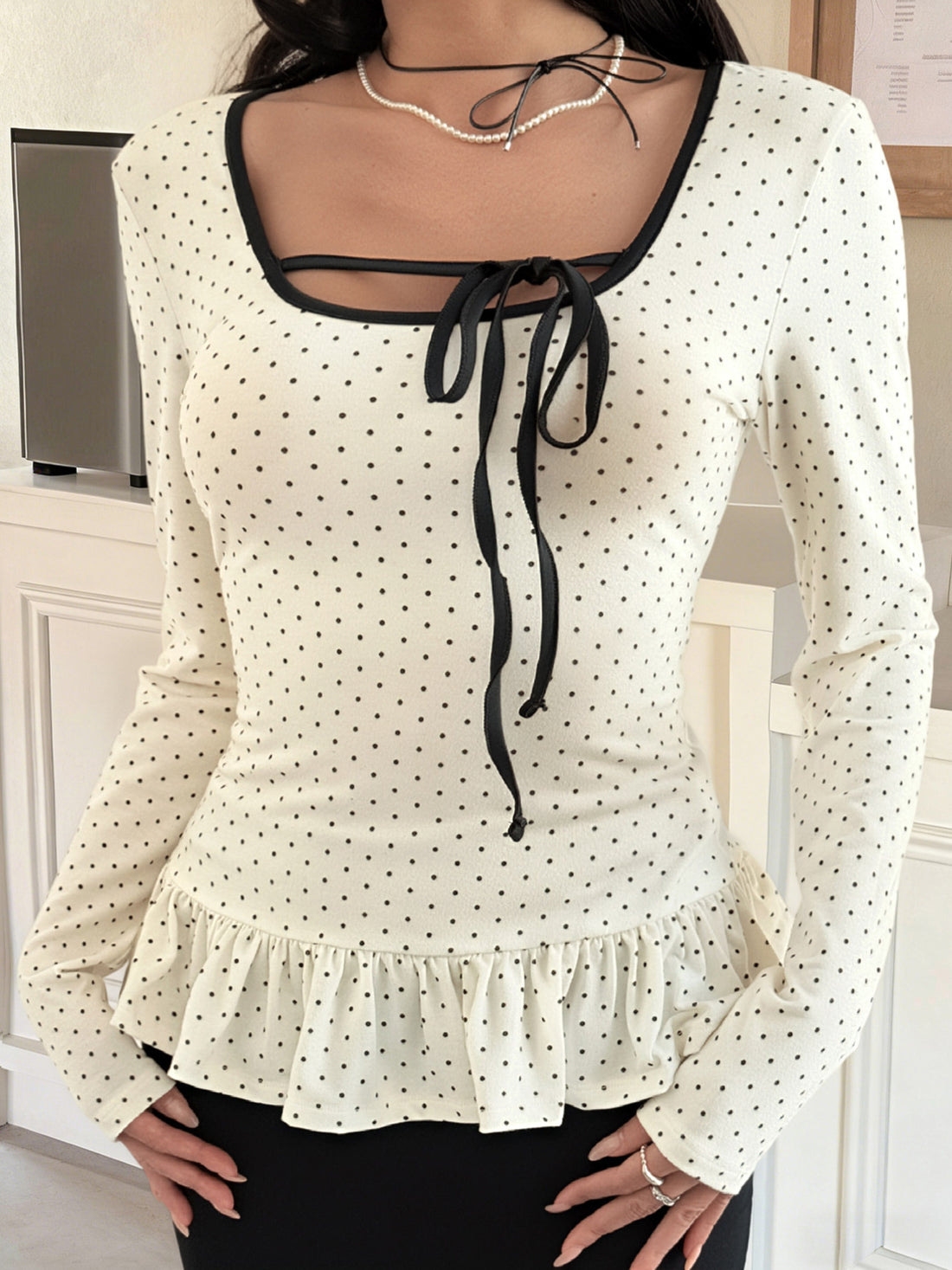 Ruffled polka dot long-sleeve t-shirt with black trim and tie-neck detail.