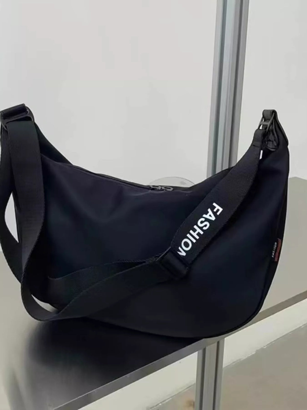 Black crossbody bag with adjustable strap and white "FASHION" text detail.